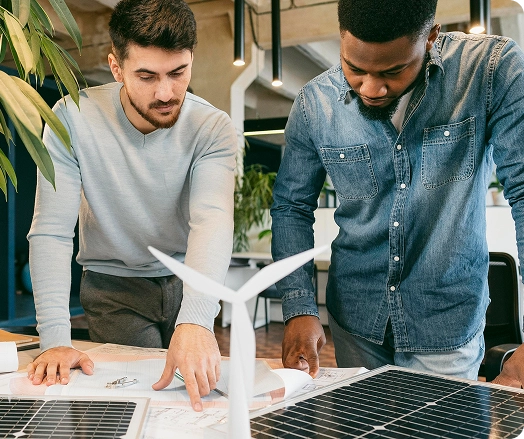 Dois profissionais colaborando no planejamento de projetos de energia renovável, revisando desenhos técnicos e layouts de sistemas solares em um ambiente de escritório moderno.